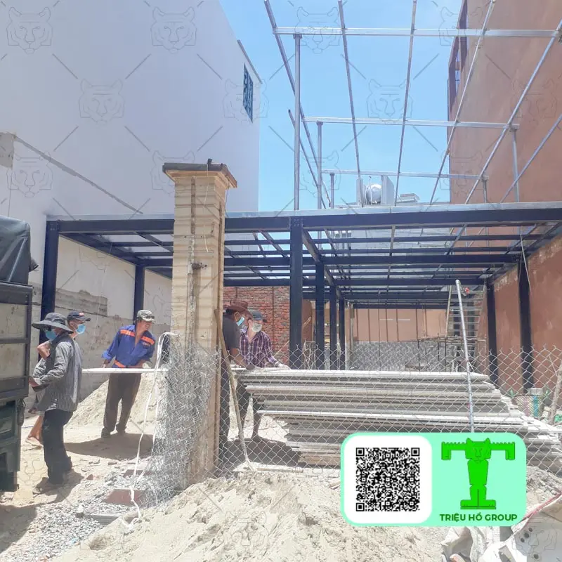 Công nhân đang vận chuyển các tấm vật liệu xây dựng tại công trường với khung thép và vật liệu tấm trần smartboard