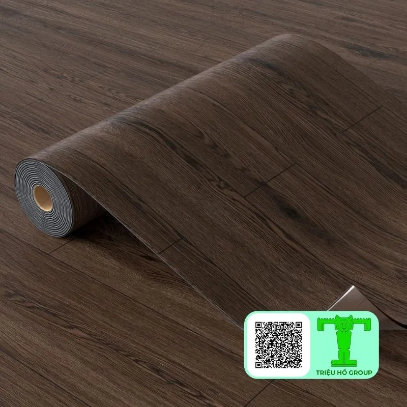Cuộn sàn nhựa vinyl màu nâu sẫm vân gỗ đang được trải ra trên nền nhà, với một phần nhỏ lớp bảo vệ được bóc ra