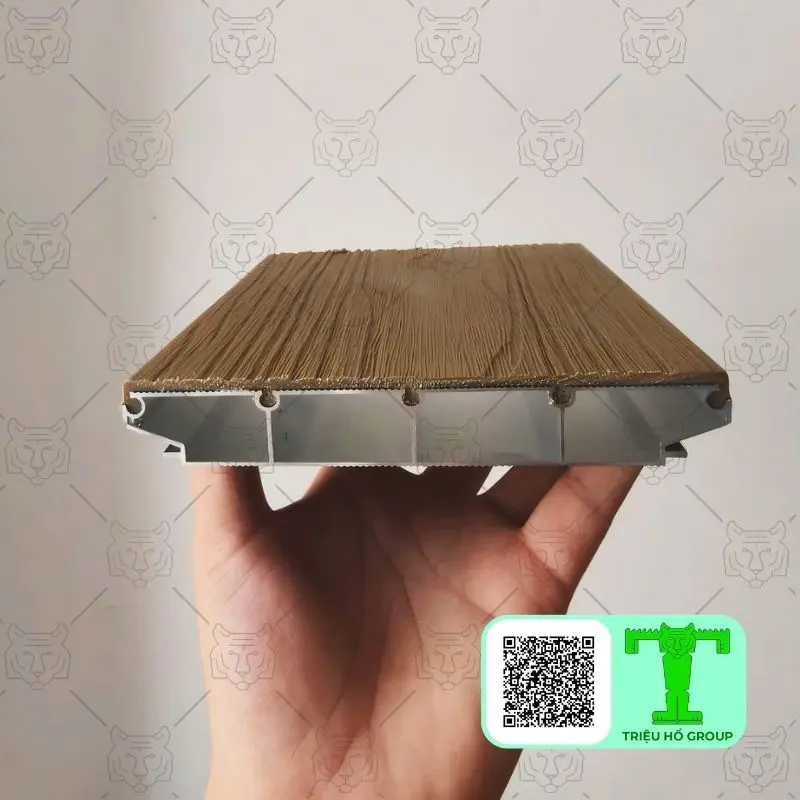 Mặt cắt của tấm sàn nhựa vân gỗ với đế hợp kim nhôm và các khoang rỗng bên trong, được một bàn tay giữ