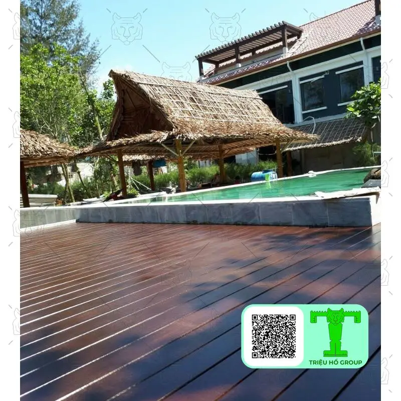 Sàn gỗ Conwood màu nâu sẫm lát cạnh hồ bơi, phía sau là các chòi lá và tòa nhà dưới trời nắng