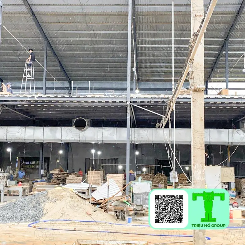 Công trường xây dựng nhà xưởng nhiều tầng với công nhân trên thang và vật liệu xây dựng như cát, sỏi