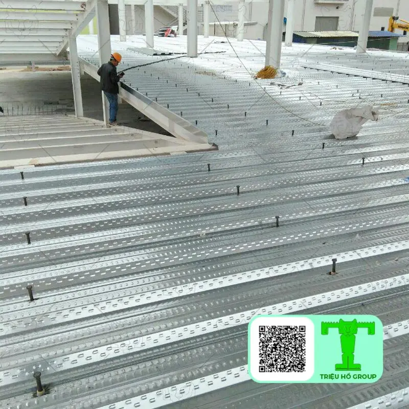 Sàn deck kim loại với đinh chống cắt đang được lắp đặt trên công trường xây dựng, có công nhân ở phía xa