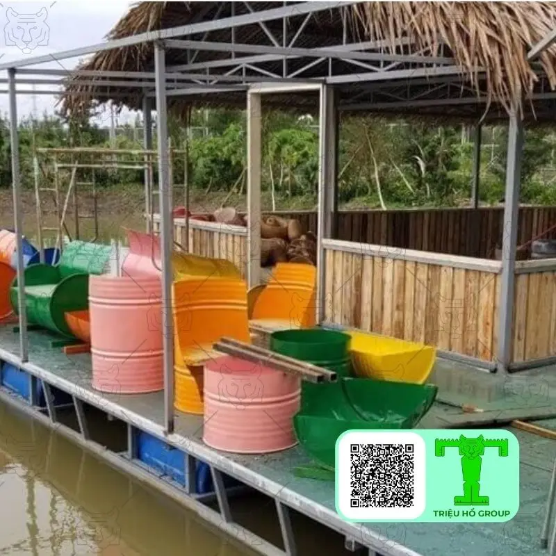 Một cấu trúc nổi trên mặt nước với mái tranh và các thùng phuy nhiều màu sắc được tái chế thành ghế hoặc vật trang trí