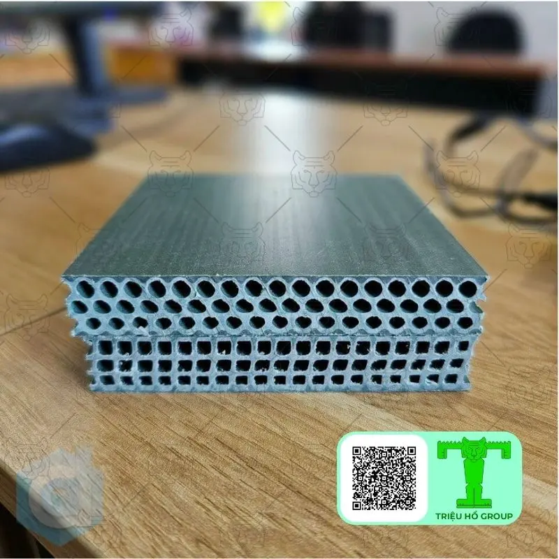 Hai mẫu ván nhựa cốp pha rỗng ruột, một loại lỗ tròn và một loại lỗ vuông, đặt trên bàn gỗ