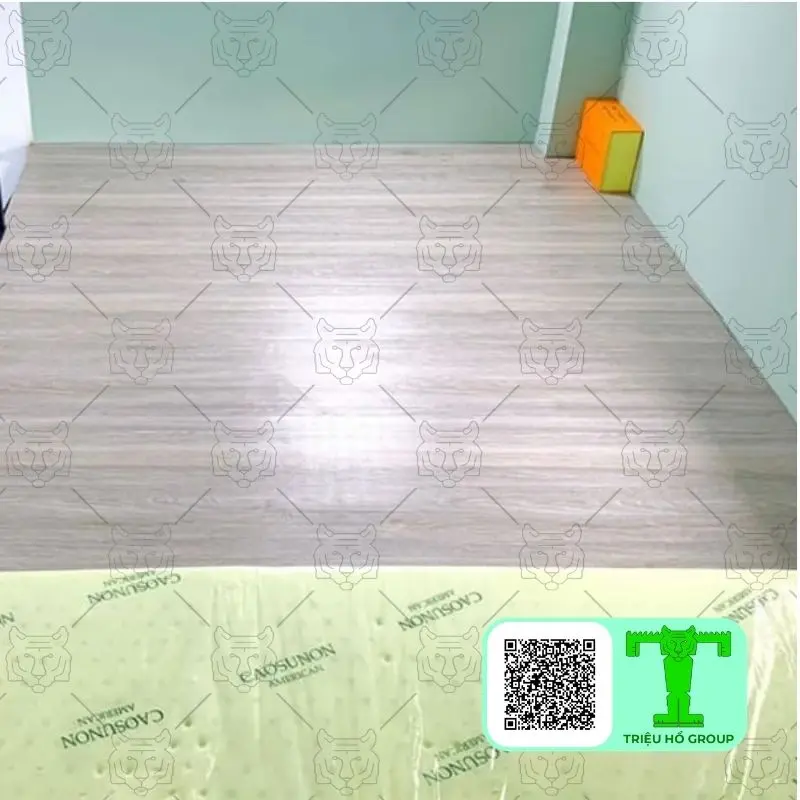Sàn nhà lát ván nhựa vân gỗ màu sáng với tường xanh nhạt và một vật thể màu cam ở góc phòng