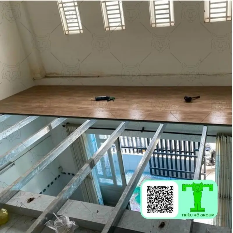 Khung thép và sàn ván nhựa đang được thi công cho gác lửng, với một phần sàn đã hoàn thiện và các dụng cụ