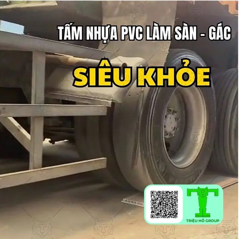 Bánh xe tải lớn đè lên tấm ván sàn nhựa PVC chịu lực, thể hiện độ bền của vật liệu, cùng dòng chữ quảng cáo và logo